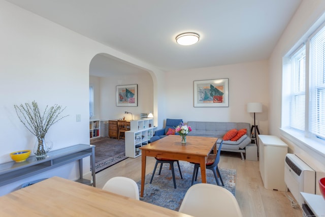 living room with arched walkways, a wall unit AC, and light wood-style floors