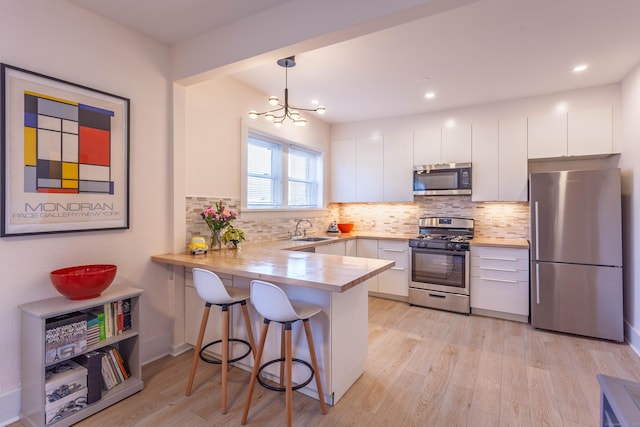 kitchen with appliances with stainless steel finishes, white cabinets, a sink, light wood-type flooring, and a peninsula