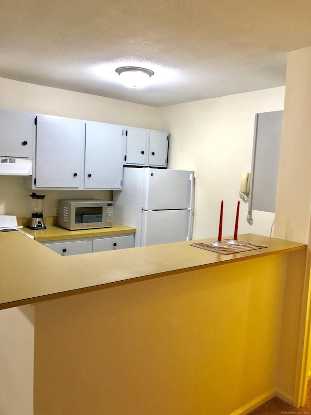 kitchen with under cabinet range hood, a peninsula, baseboards, light countertops, and freestanding refrigerator