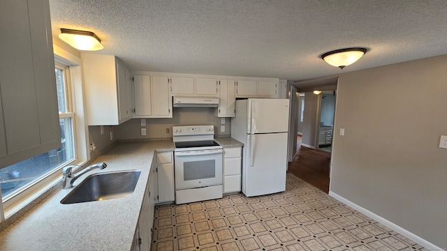 kitchen featuring white appliances, light floors, light countertops, under cabinet range hood, and a sink