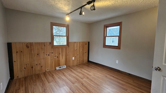 spare room featuring visible vents, wainscoting, wood finished floors, a textured ceiling, and wood walls