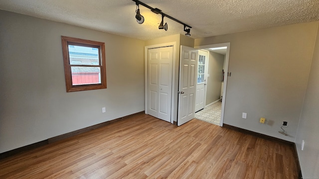 unfurnished bedroom featuring light wood-type flooring, a closet, baseboards, and a textured ceiling