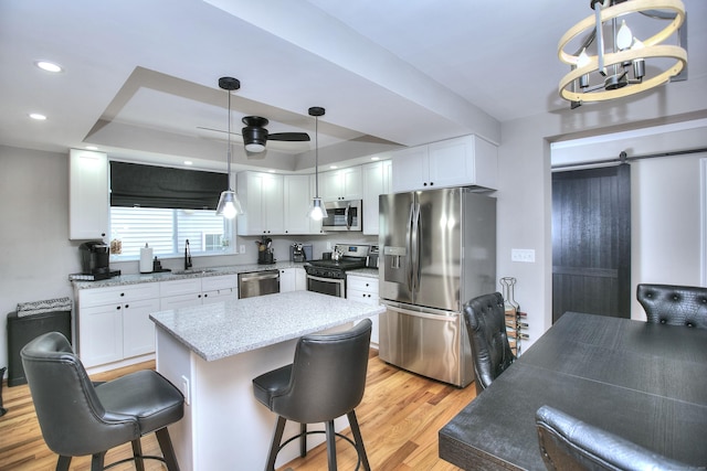 kitchen with light wood-style flooring, stainless steel appliances, a sink, white cabinets, and a raised ceiling