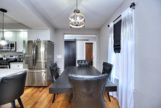 dining area featuring light wood finished floors, a barn door, and an inviting chandelier