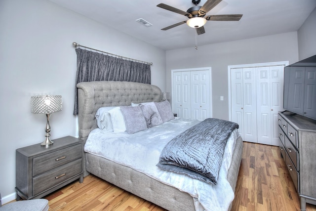 bedroom featuring ceiling fan, light wood finished floors, two closets, and visible vents