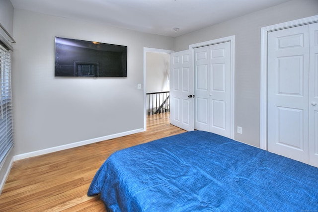 bedroom with multiple closets, wood finished floors, and baseboards