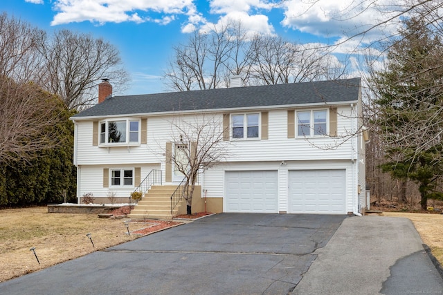 split foyer home featuring an attached garage, a chimney, and aphalt driveway