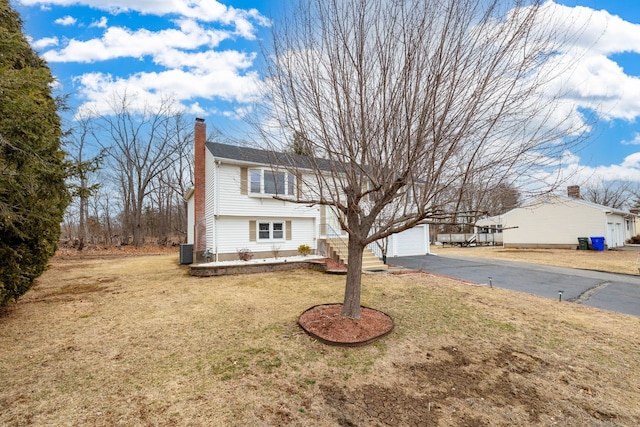 view of front of property featuring a garage, a chimney, a front lawn, and central AC unit