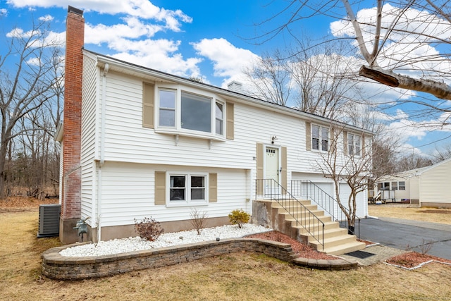 bi-level home featuring a garage, central AC, aphalt driveway, and a chimney