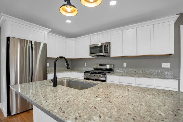 kitchen with appliances with stainless steel finishes, white cabinets, a sink, and light stone counters