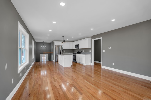 unfurnished living room featuring a chandelier, light wood-type flooring, baseboards, and recessed lighting