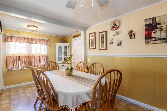 dining space featuring ceiling fan, a wainscoted wall, and ornamental molding