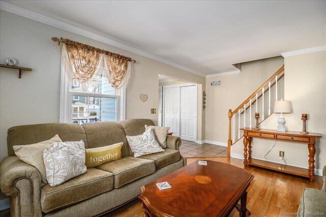 living area featuring stairs, baseboards, light wood finished floors, and ornamental molding