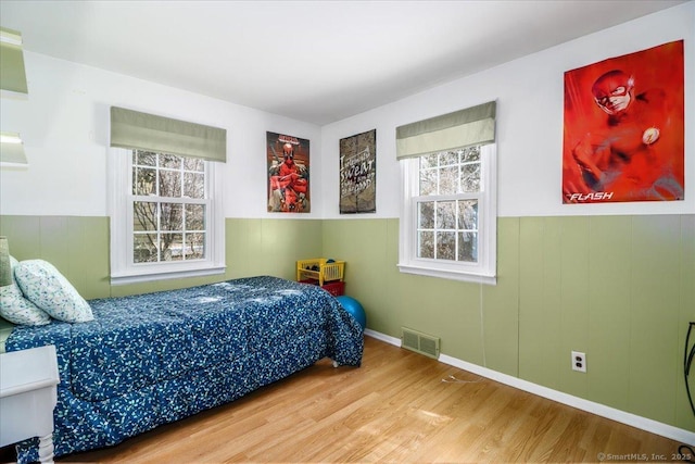 bedroom featuring a wainscoted wall, multiple windows, visible vents, and wood finished floors