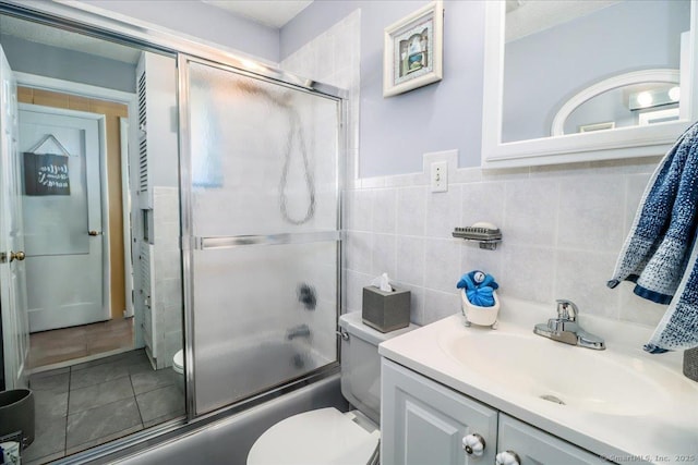 full bathroom with tile patterned floors, toilet, tile walls, bath / shower combo with glass door, and vanity