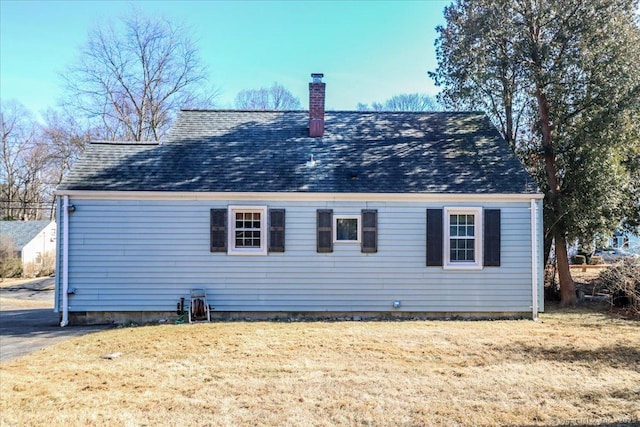 back of property featuring a lawn, roof with shingles, and a chimney