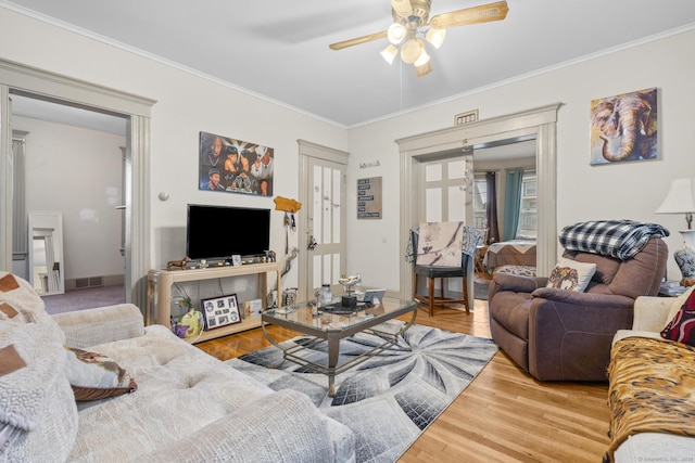 living area with ceiling fan, wood finished floors, visible vents, baseboards, and ornamental molding