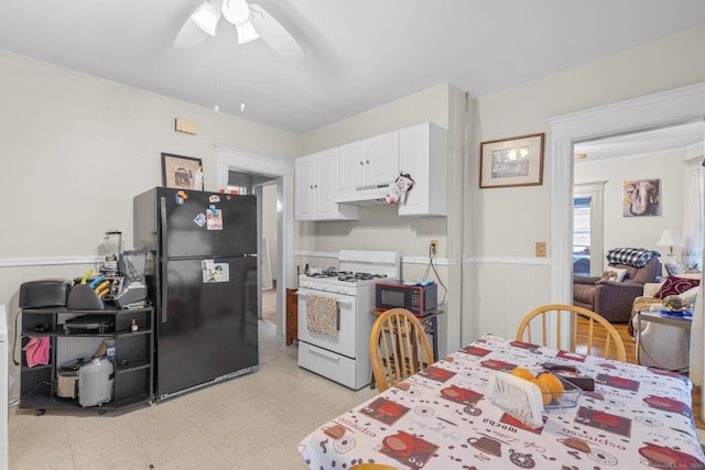 kitchen with white cabinets, wainscoting, freestanding refrigerator, white gas range, and under cabinet range hood