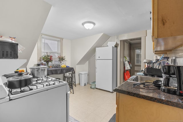 kitchen featuring light floors, white appliances, dark countertops, and a sink