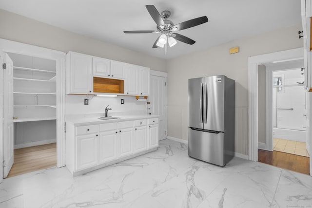 kitchen featuring white cabinets, freestanding refrigerator, marble finish floor, light countertops, and a sink