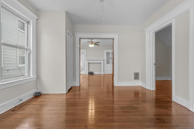 empty room featuring a ceiling fan, visible vents, baseboards, and wood finished floors