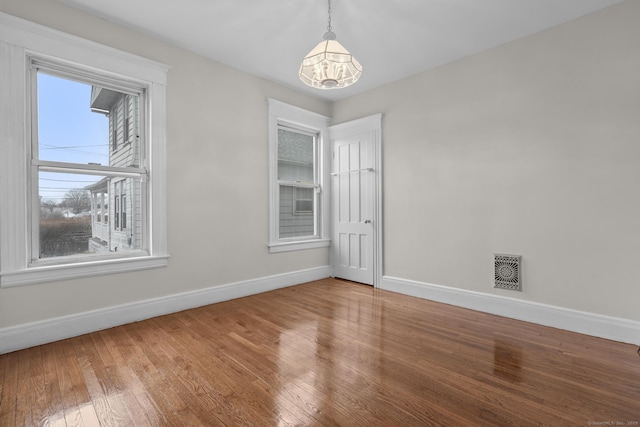 unfurnished room with baseboards, visible vents, a chandelier, and hardwood / wood-style floors