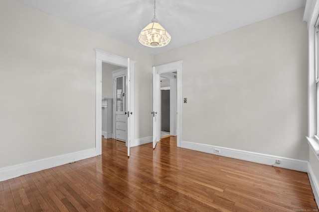 spare room featuring wood-type flooring, baseboards, and a notable chandelier