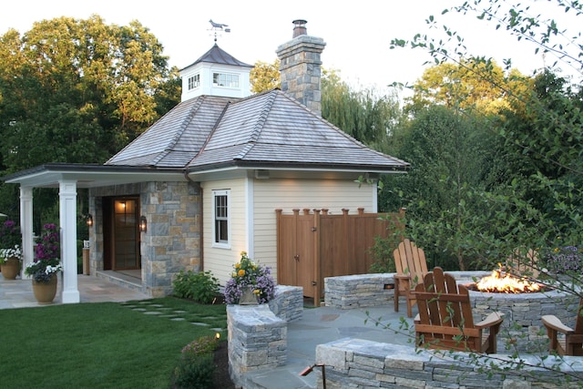 rear view of property featuring a lawn, stone siding, a fire pit, a chimney, and a patio area