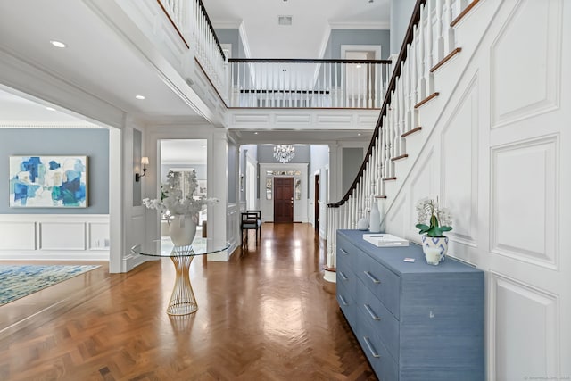 foyer featuring stairs, crown molding, a decorative wall, and a towering ceiling