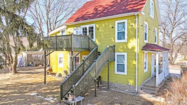 back of property featuring roof with shingles, an outdoor structure, stairs, and a shed