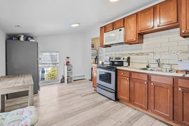 kitchen featuring light countertops, brown cabinets, light wood-style floors, stainless steel appliances, and a sink