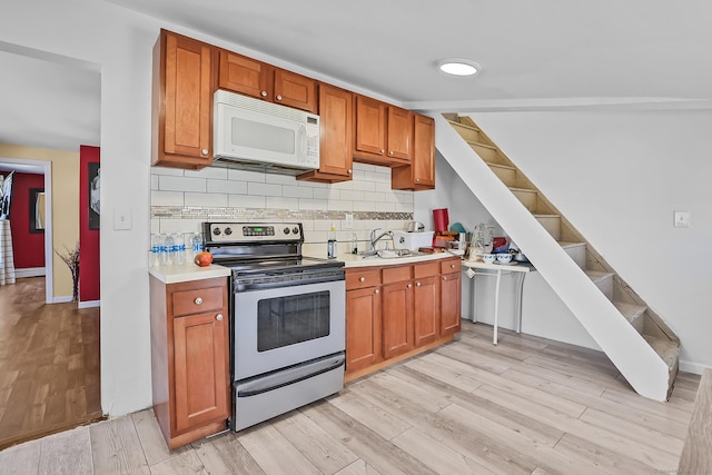 kitchen with stainless steel electric range oven, white microwave, light wood-style flooring, a sink, and decorative backsplash