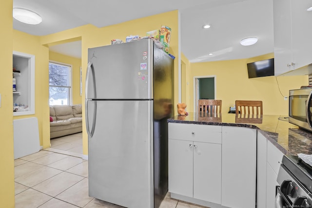 kitchen with light tile patterned flooring, white cabinets, appliances with stainless steel finishes, and dark stone counters