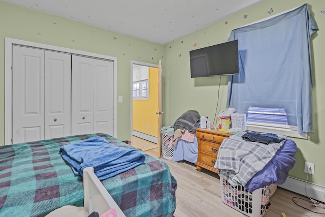 bedroom with a closet, baseboard heating, a baseboard radiator, and wood finished floors