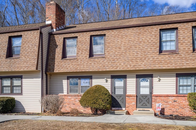 townhome / multi-family property featuring brick siding, roof with shingles, and a chimney