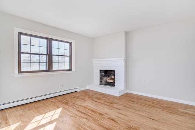 unfurnished living room featuring baseboards, baseboard heating, light wood-type flooring, and a brick fireplace