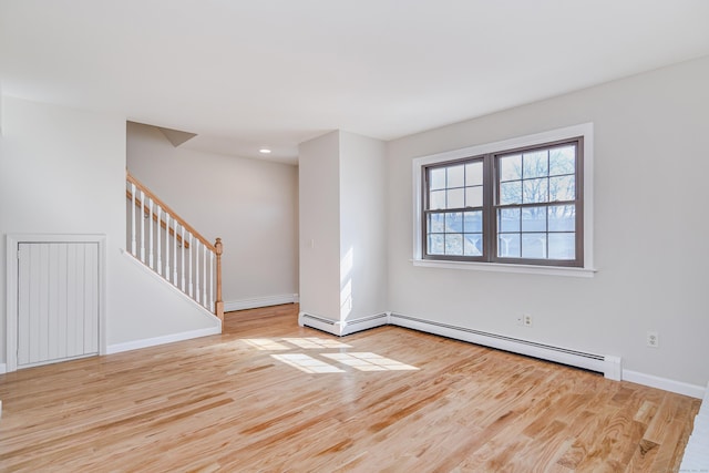 spare room with stairs, a baseboard radiator, wood finished floors, and baseboards