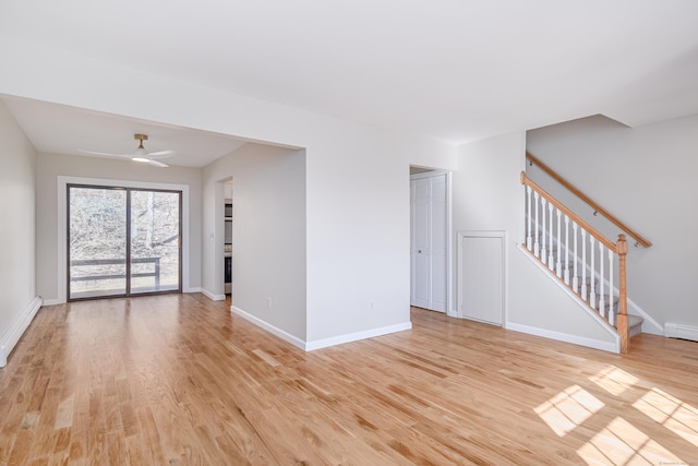 empty room featuring light wood-type flooring, stairs, and a baseboard heating unit