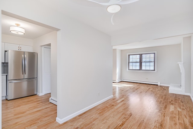 interior space with white cabinets, light wood finished floors, baseboard heating, and freestanding refrigerator