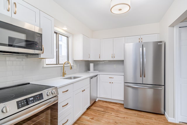 kitchen with light wood finished floors, stainless steel appliances, light countertops, white cabinetry, and a sink