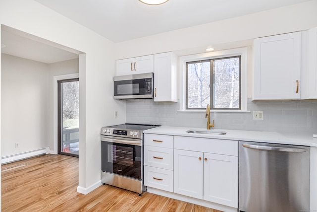 kitchen with light wood finished floors, stainless steel appliances, light countertops, a baseboard heating unit, and a sink