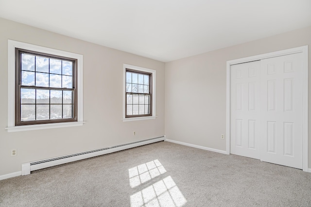 unfurnished bedroom with baseboard heating, carpet, a closet, and baseboards