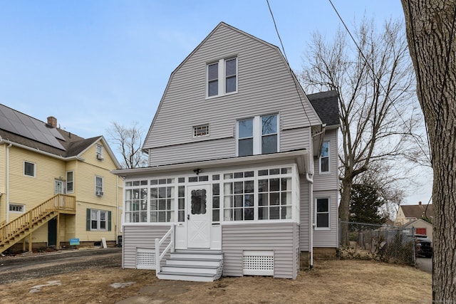 rear view of house featuring solar panels, a shingled roof, fence, a sunroom, and a gambrel roof