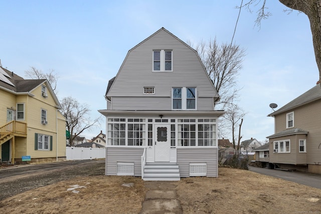 view of front of home featuring entry steps, a sunroom, and a gambrel roof