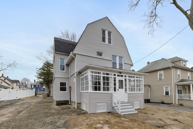 back of property featuring a shingled roof, a gambrel roof, entry steps, a sunroom, and fence