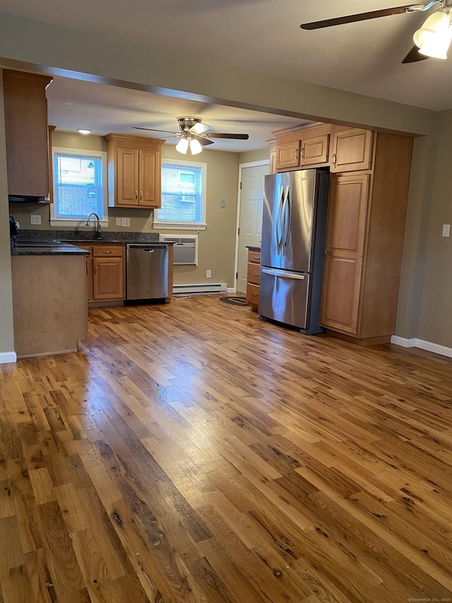 kitchen with a wealth of natural light, dark countertops, wood finished floors, appliances with stainless steel finishes, and ceiling fan