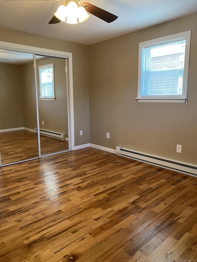 unfurnished bedroom featuring a baseboard radiator, baseboards, a closet, and wood finished floors