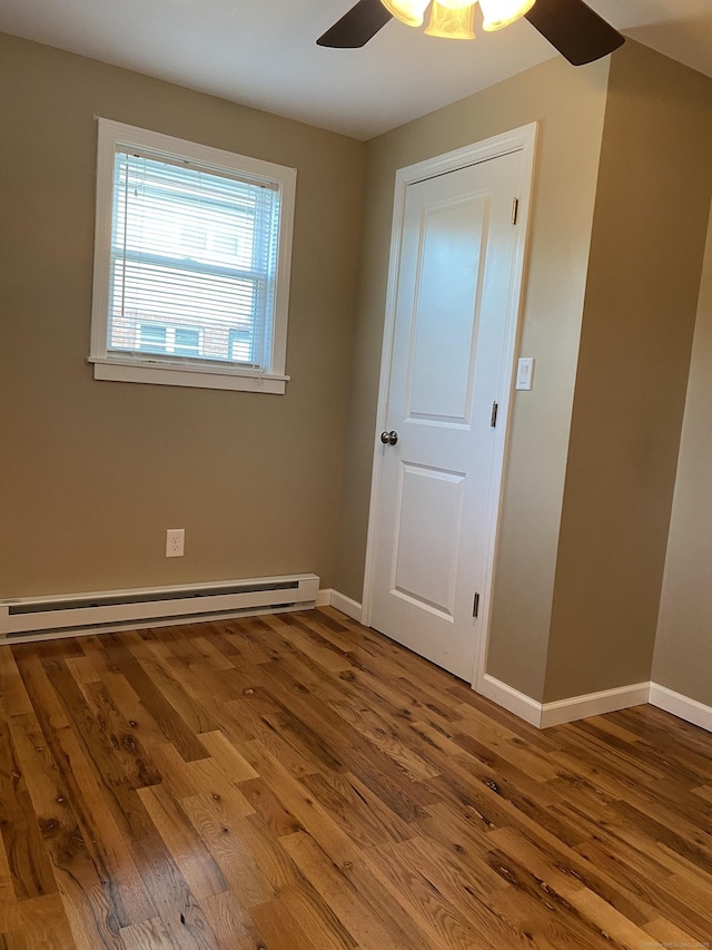 unfurnished bedroom featuring ceiling fan, a baseboard heating unit, baseboards, and wood finished floors