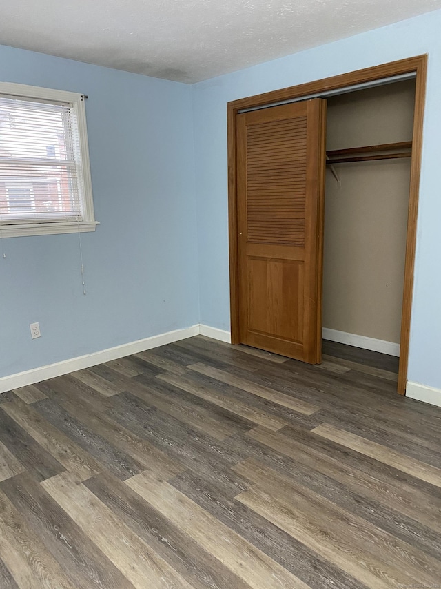 unfurnished bedroom with a closet, baseboards, and dark wood-style floors