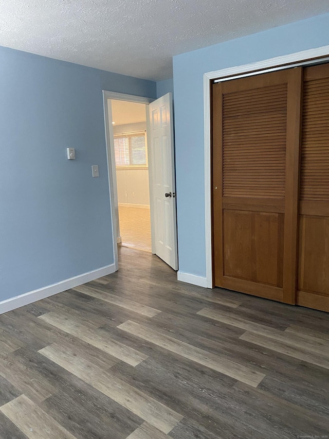 unfurnished bedroom featuring a closet, baseboards, a textured ceiling, and dark wood finished floors